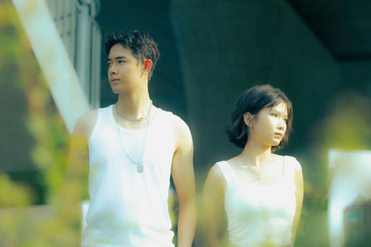 Asian couple in white tank tops standing outside with a thoughtful gaze.