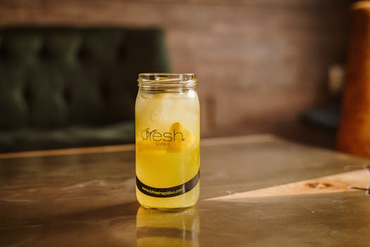 Chilled lemonade in a mason jar with lemon slices on a wooden table indoors.
