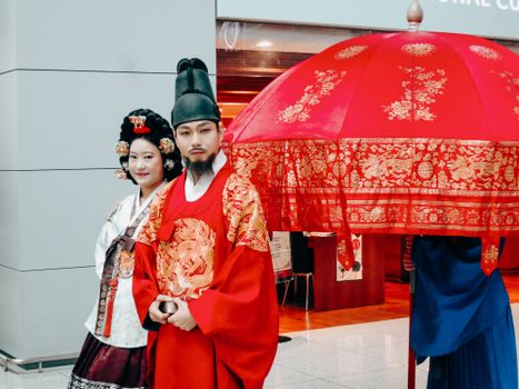 A couple dressed in traditional Korean royal attire with a beautiful red parasol. Captivating cultural attire.