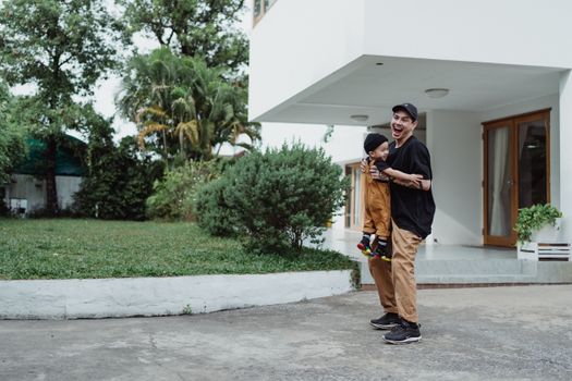 A joyful father and son play together in a sunny outdoor front yard setting, capturing family togetherness.