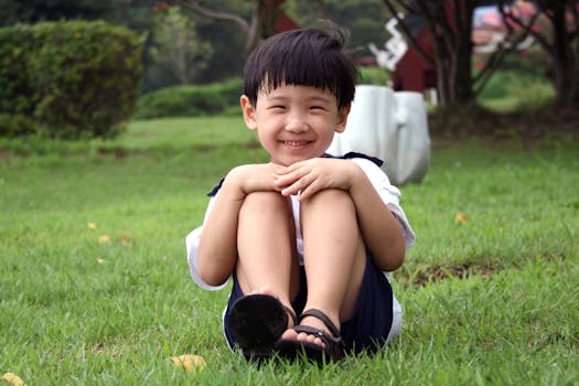 Smiling boy sitting cross-legged on the grass, enjoying a sunny day outdoors.
