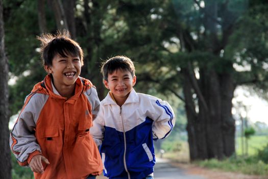 Two East Asian boys happily running on a rural path in Gia Lai, Vietnam.